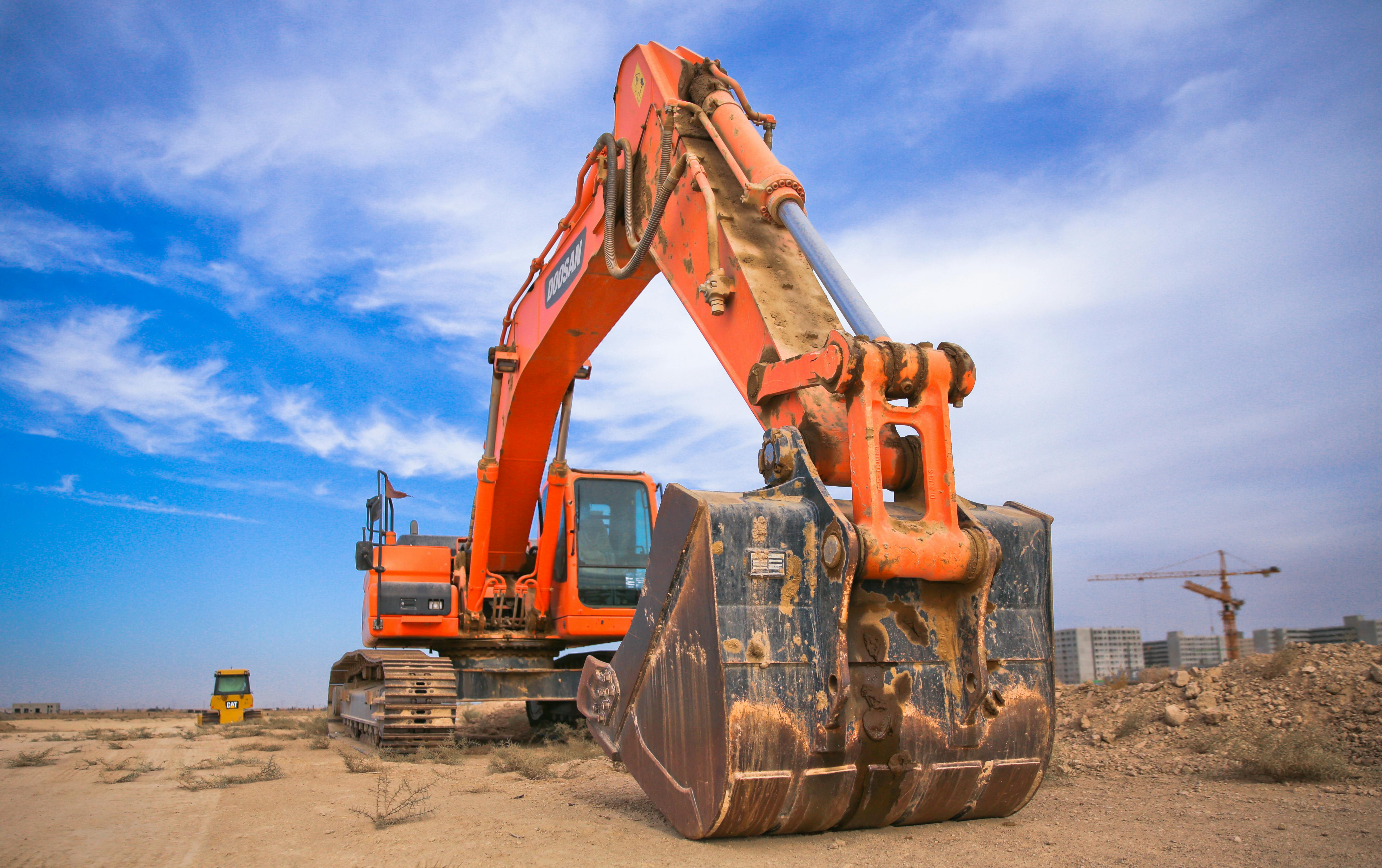 Orange excavator under a blue sky with clouds